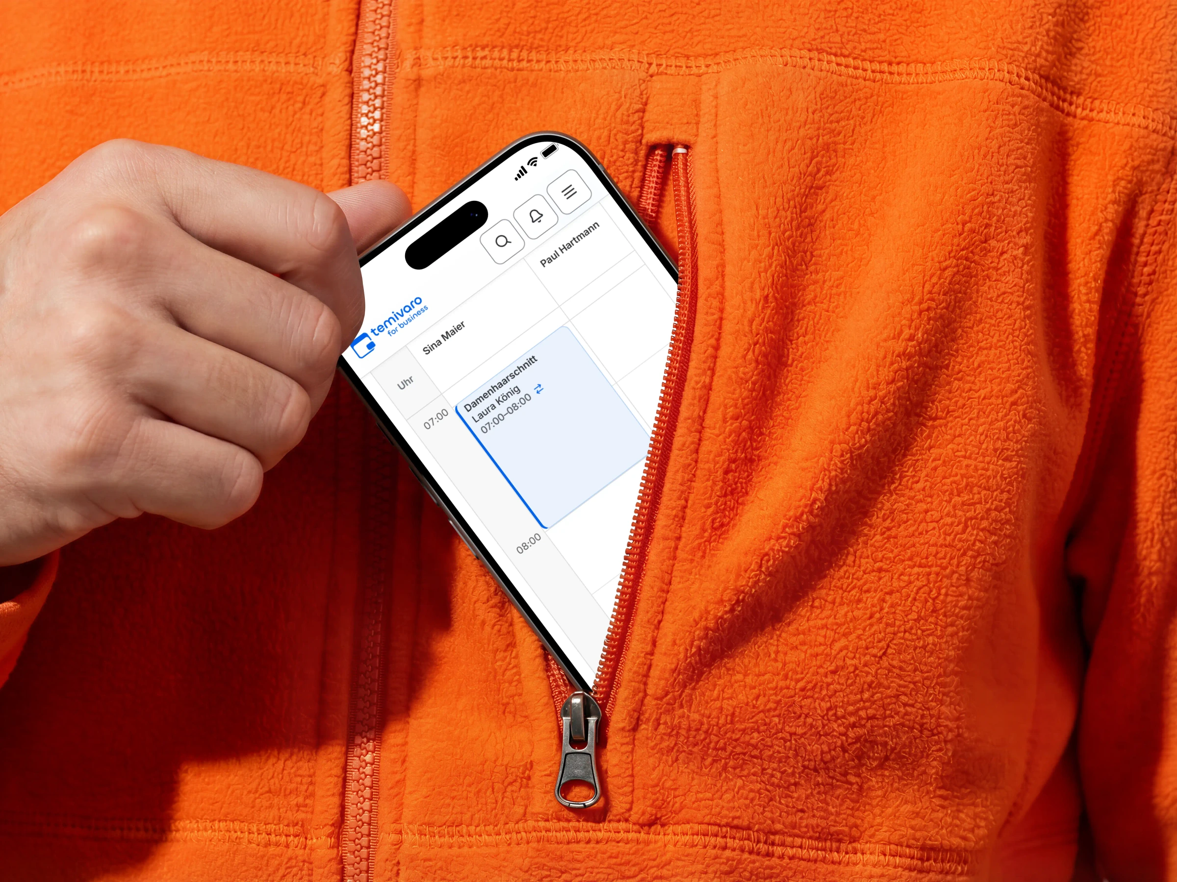 Smartphone mit dem Temivaro-Terminkalender in einer orangefarbenen Jackentasche